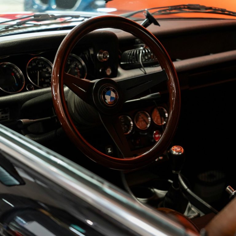 Interieur eines klassischen BMW mit Holzlenkrad und sportlichen Instrumenten.